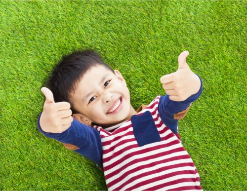 a child lying on the grass showing two thumbs up